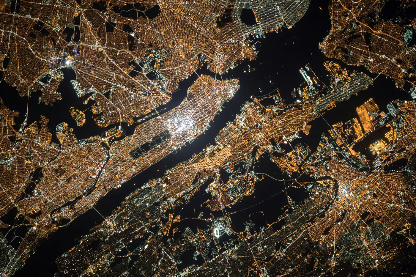 Nueva York de noche vista desde la órbita: el alumbrado dibuja la trama de calles manzana a manzana y los ríos quedan en negro